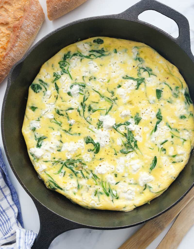 Top view of a black skillet containing a freshly baked arugula frittata with feta.