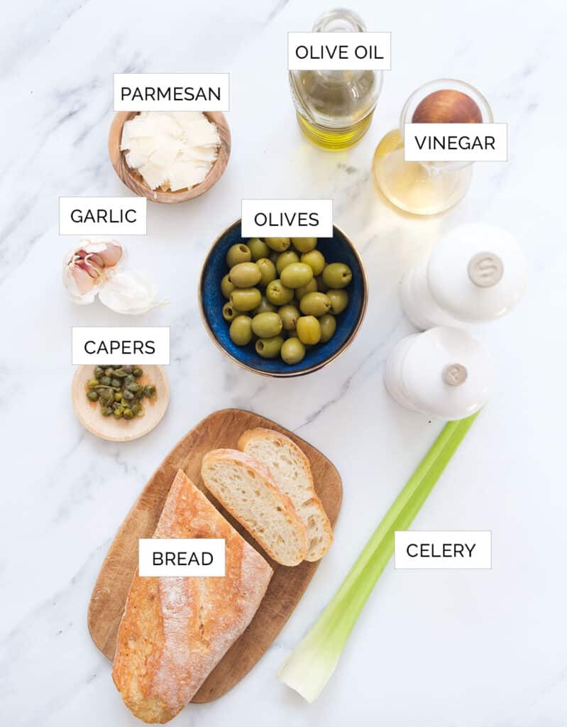 The ingredients to make this olive bruschetta are arranged over a white background.