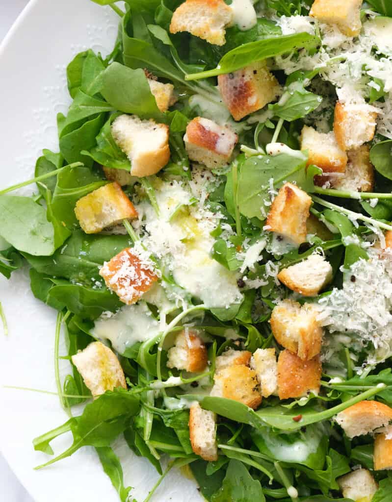 Close-up of some spinach arugula salad with the creamy lemon yogurt dressing and crispy croutons.