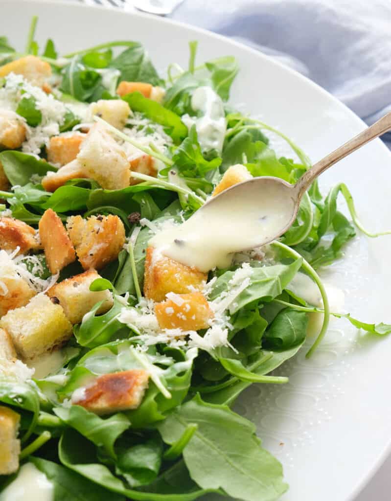A spoon pouring the yogurt dressing over the spinach arugula salad.