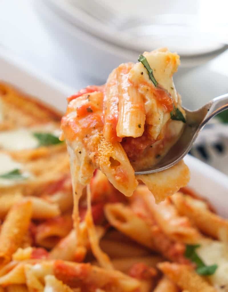 Close-up of a fork full of baked penne in tomato sauce with melted mozzarella.