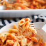 Close-up of a white bowl full of baked penne pasta.