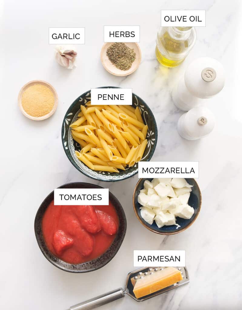 The ingredients to make this baked penne pasta are arranged over a white background.