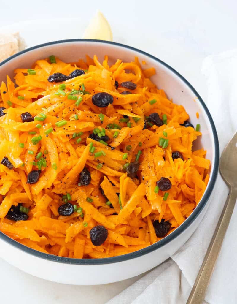 A white bowl full of carrot raisin salad.