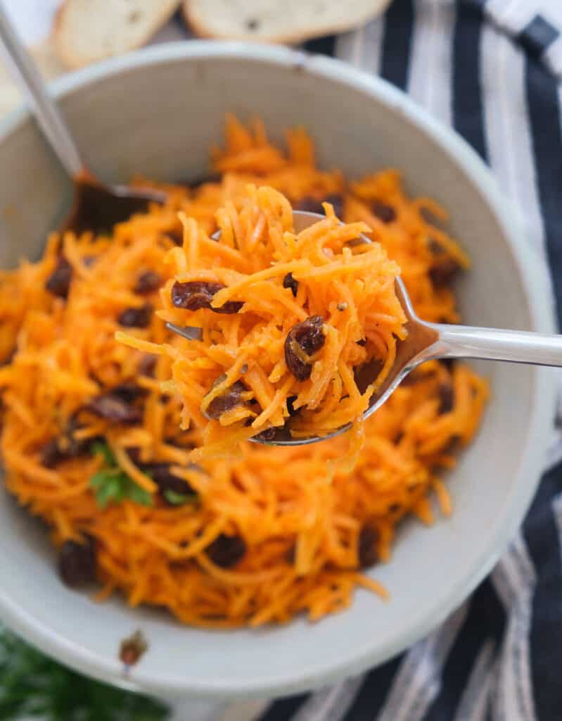 Top view of a bowl with carrot raisin salad over a black and white kitchen towel.