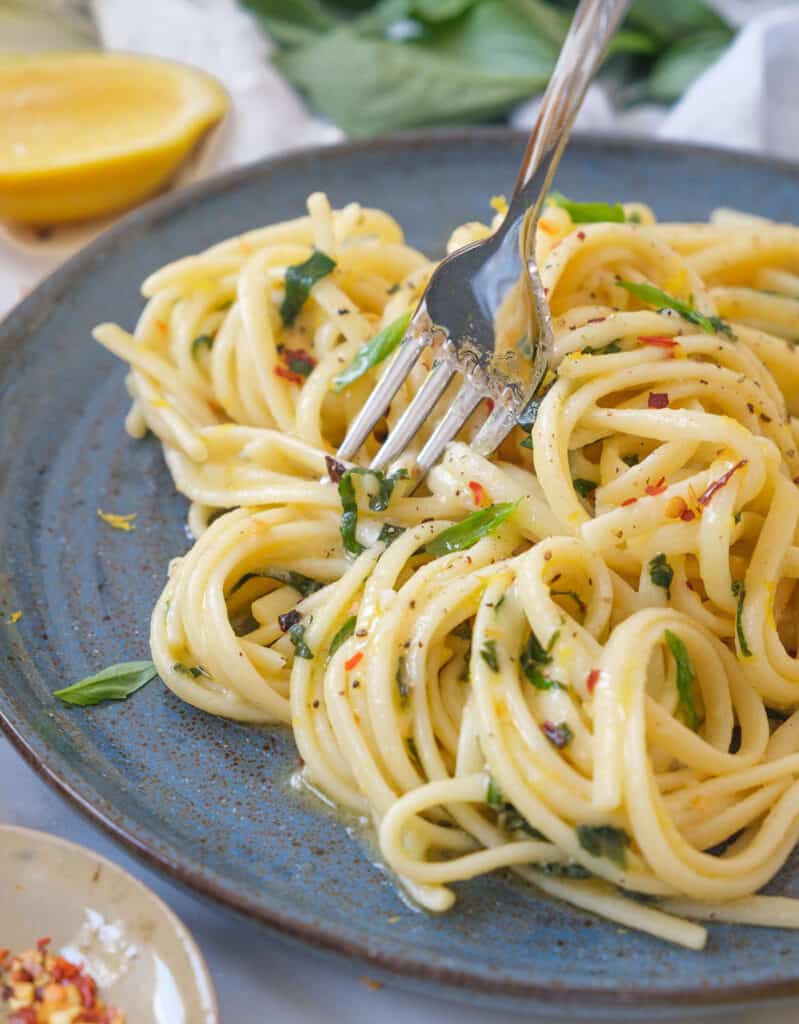Close-up of a fork and lemon garlic pasta on a blue plate.