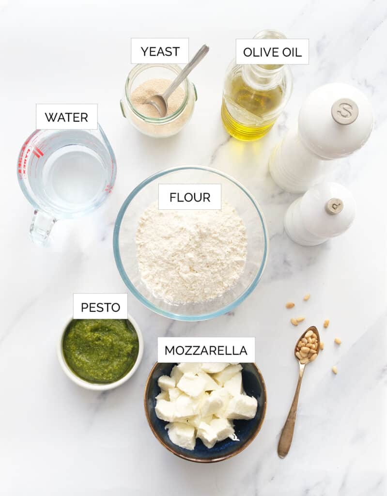이 페스토 피자를 만들기 위한 재료는 흰색 배경 위에 배열되어 있습니다.