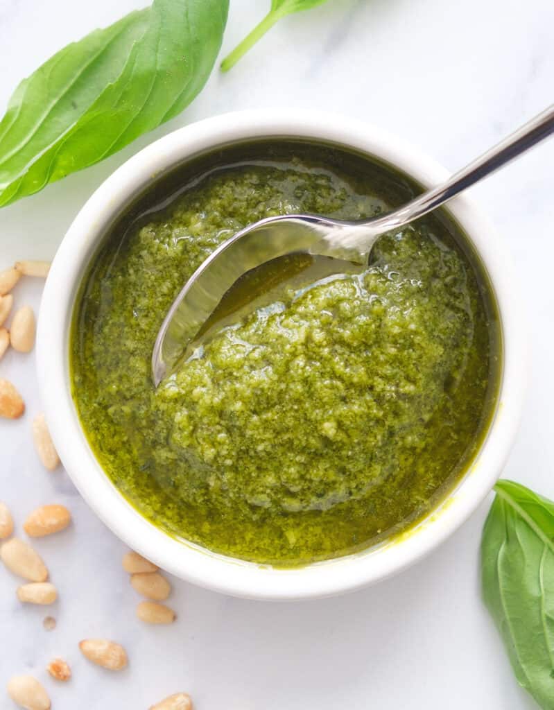 Top view of a white bowl full of fresh basil pesto sauce over a white background.