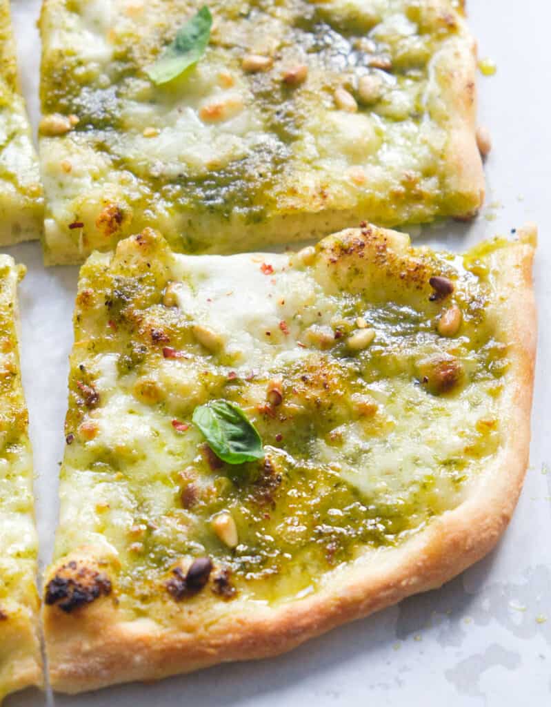 Close-up of some pesto pizza over a white background.