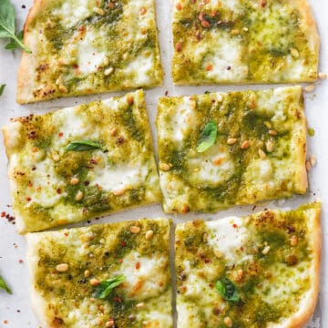 Top view of a large pesto pizza cut into slices.