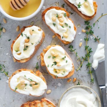 Top view of several ricotta crostini drizzled with honey and sprinkled with pine nuts.