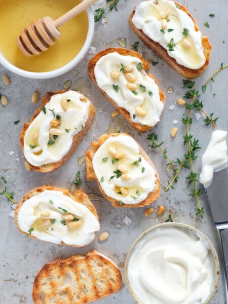 Top view of several ricotta crostini drizzled with honey and sprinkled with pine nuts.