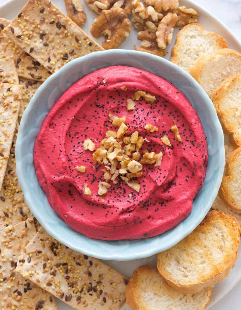 Top view of a light blue bowl full of beet hummus served with crackers.
