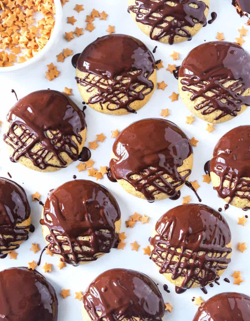 Top view of many chocolate orange cookies over a white background and scattered stars sprinkles.