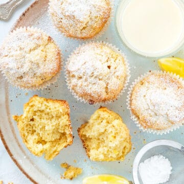 Top view of a light blue plate with several cream cheese muffins dusted with powdered sugar.