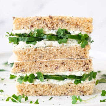 Close up of 2 cream cheese sandwiches with cucumber over a white background.