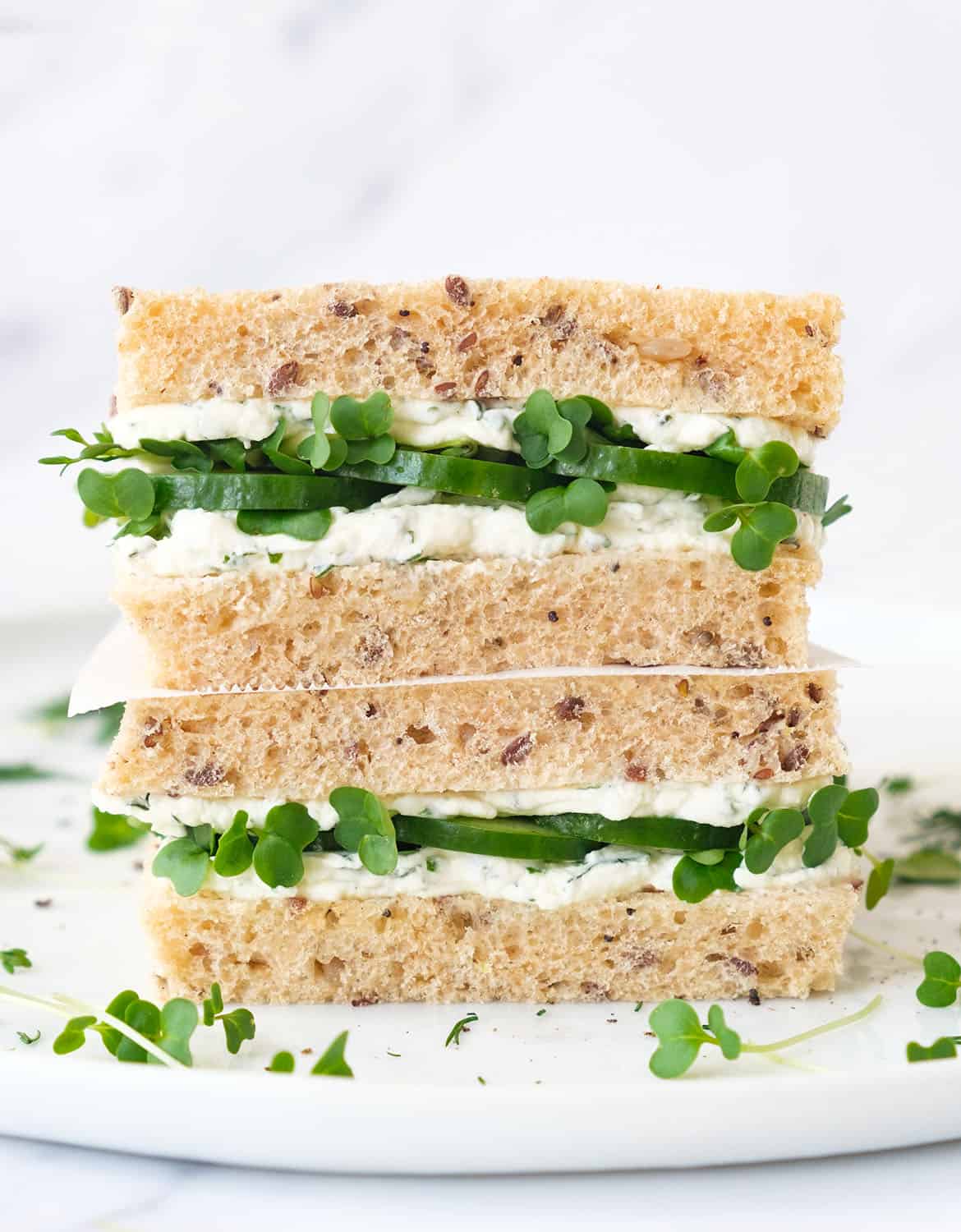 Close-up of a multigrain cream cheese sandwich with cucumber over a white background.