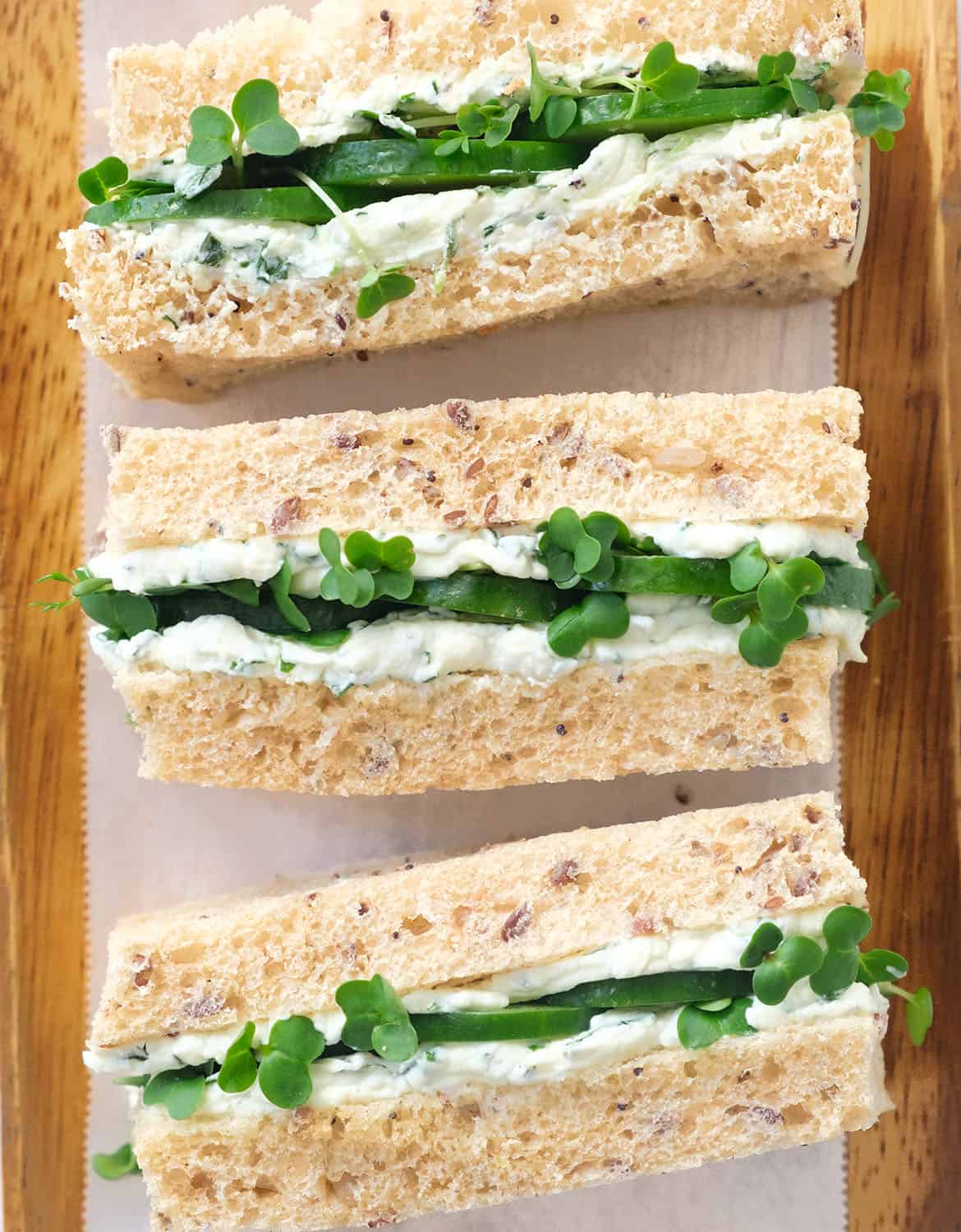 Close-up of three mini cream cheese sandwiches arranged over a wooden tray.