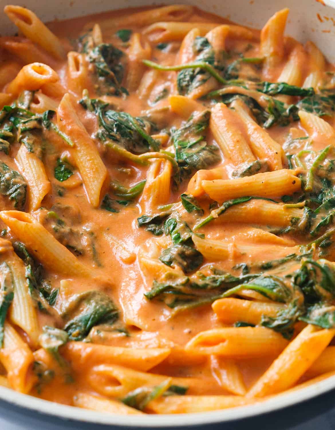 Close-up of a skillet full of creamy tomato spinach pasta coated in velvety sauce.