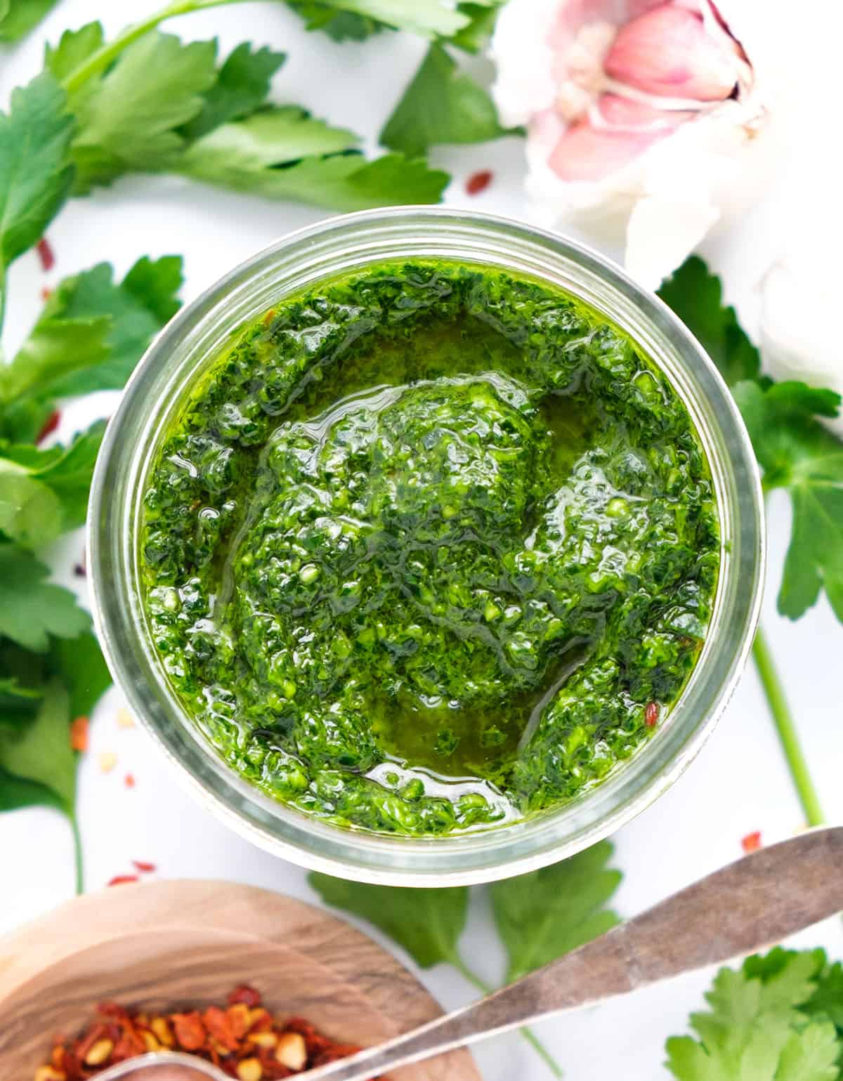 Top view of a glass jar full of parsley pesto over a white background.