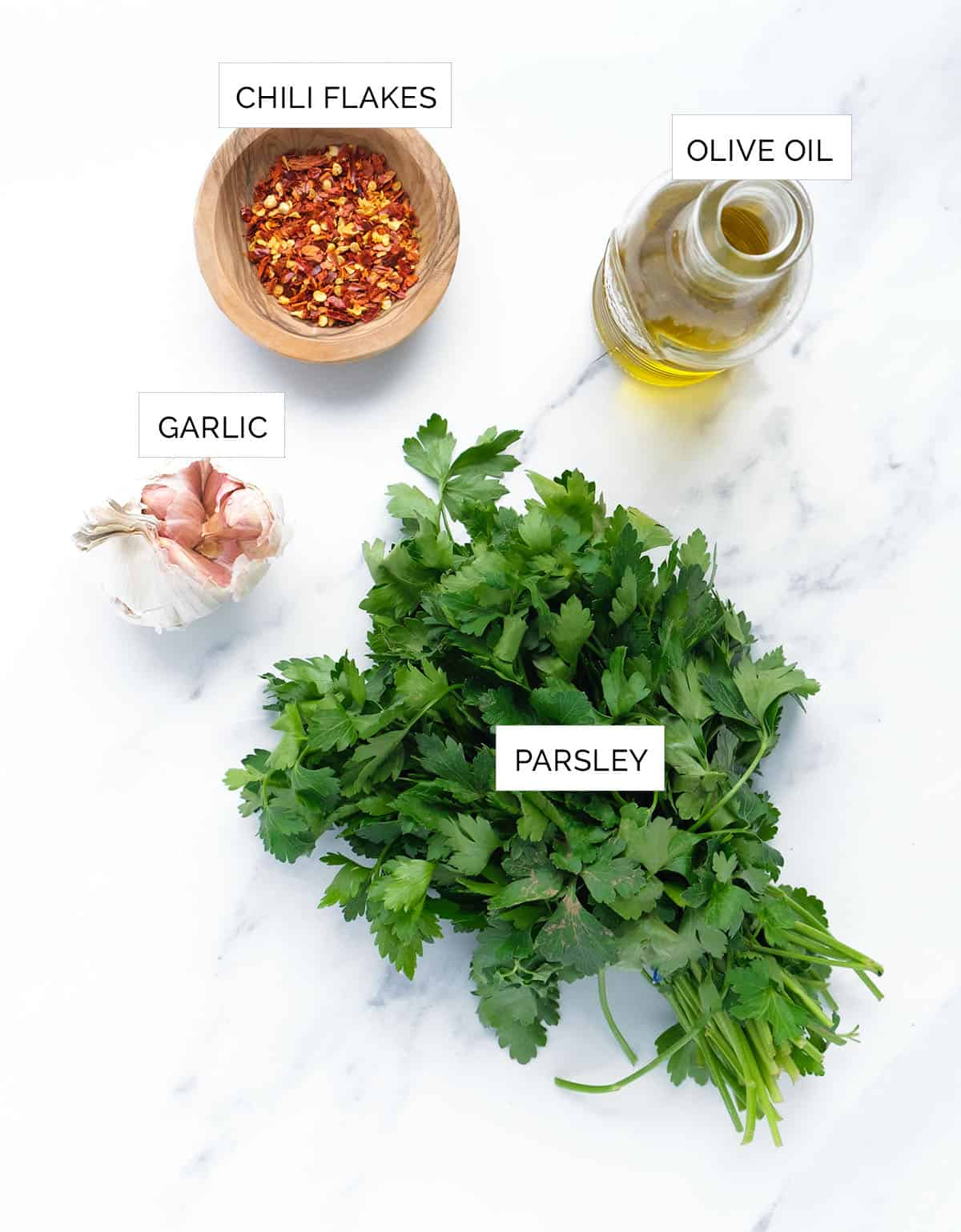 The ingredients to make parsley pesto are arranged over a white background.