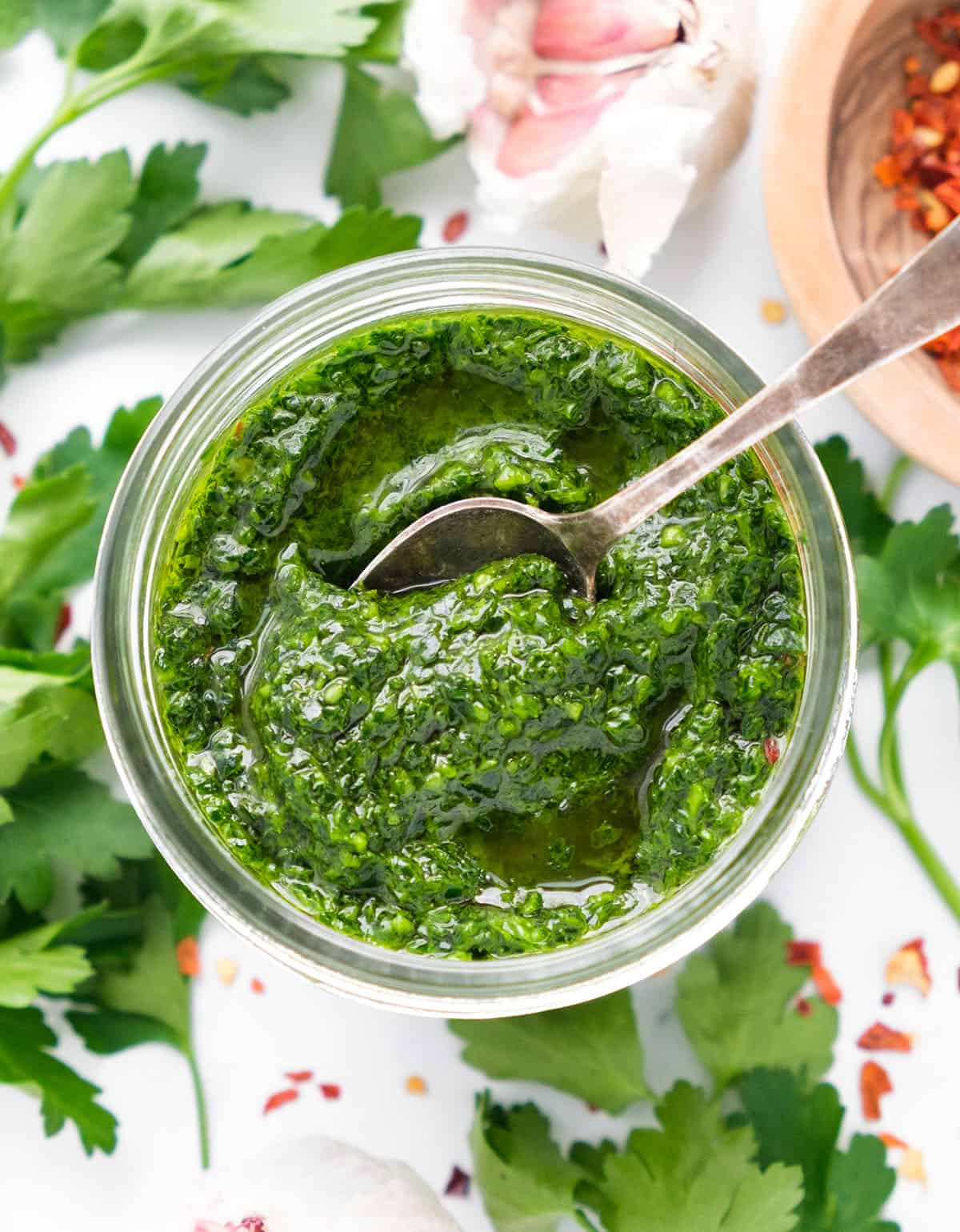 Top view of a glass jar full of parsley pesto with a spoon.