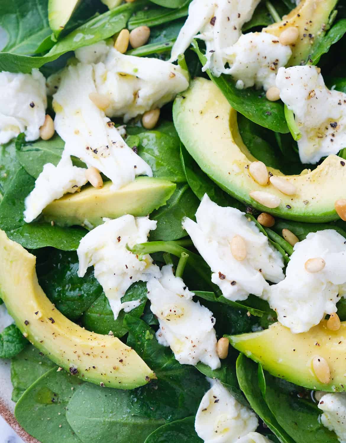 Close-up of some spinach avocado salad with fresh mozzarella and toasted pine nuts.