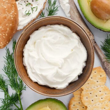 Top view of a brown bowl full of whipped cream cheese served with bagels and avocado.