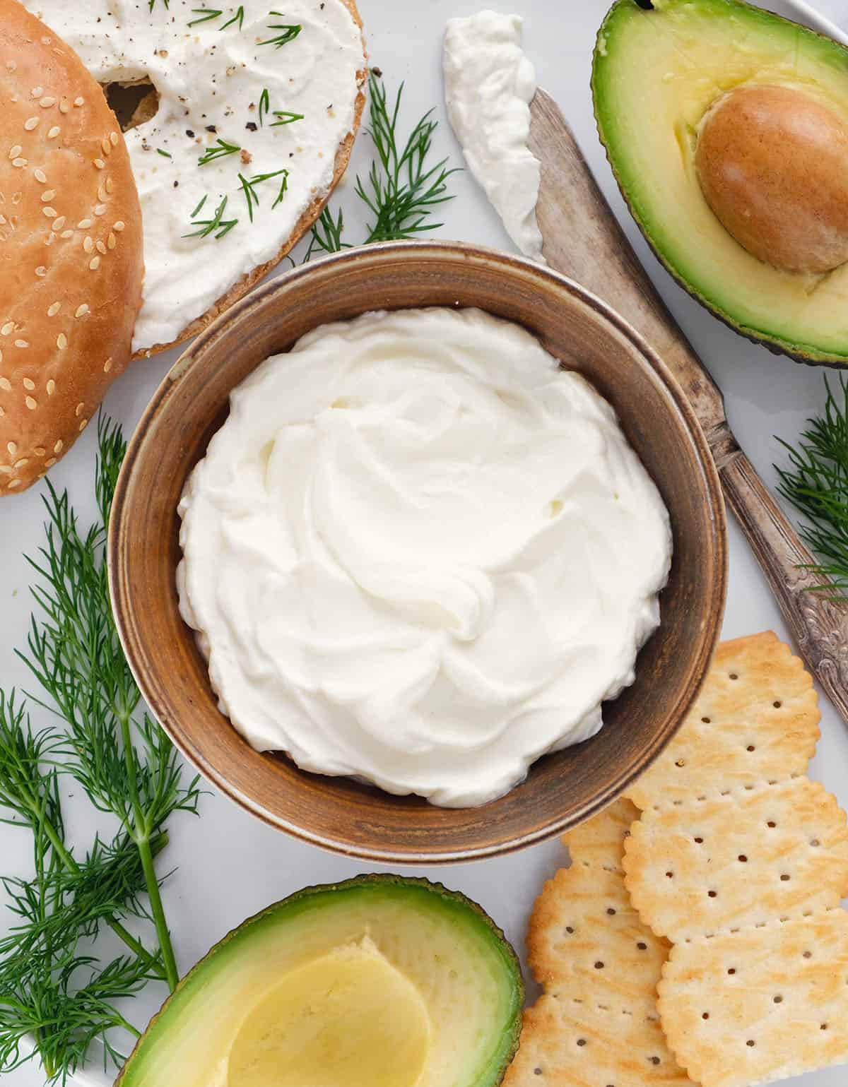 Top view of a brown bowl full of whipped cream cheese served with bagels and avocado.