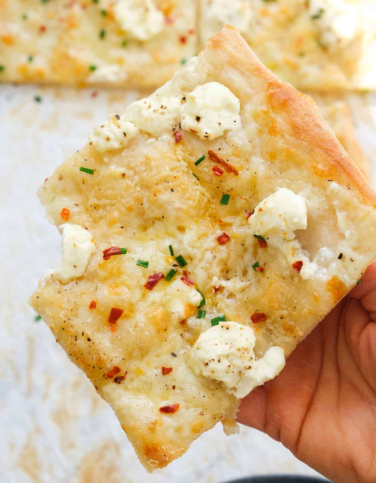 A slice of cream cheese pizza with chili flakes showing its soft, creamy texture.