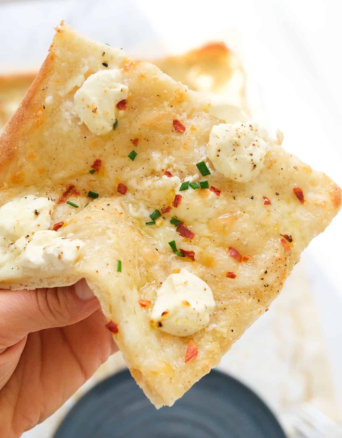 A slice of cream cheese pizza with chili flakes showing its soft, creamy texture.