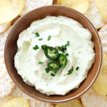 Top view of a brown bowl full of jalapeño cream cheese served with crackers.