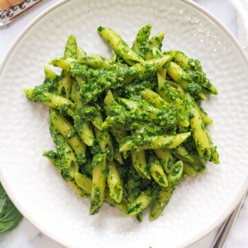 Top view of some spinach pesto pasta served on a white plate.