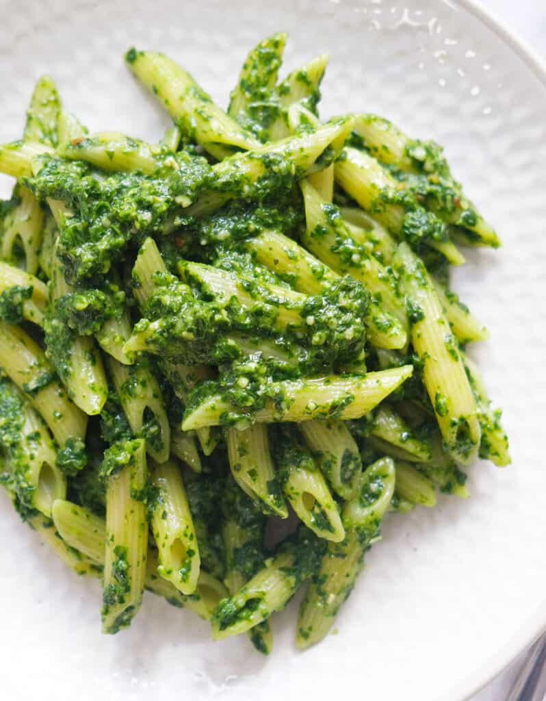 Top view of some spinach pesto pasta over a white plate.