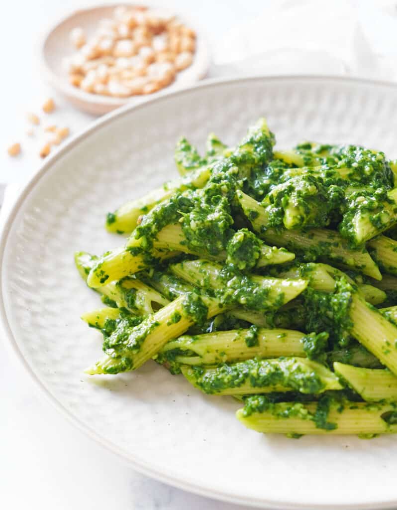 Close-up of some spinach pesto pasta served on a white plate over a white background.