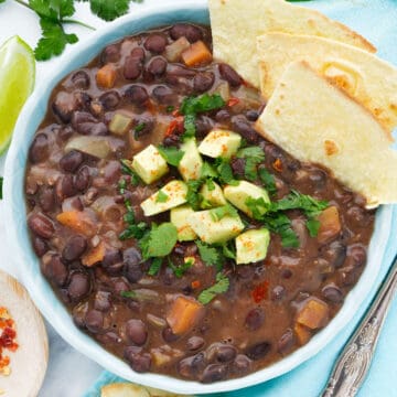 Top view of a turquoise bowl full of vegan black bean soup served with tortilla and avocado.