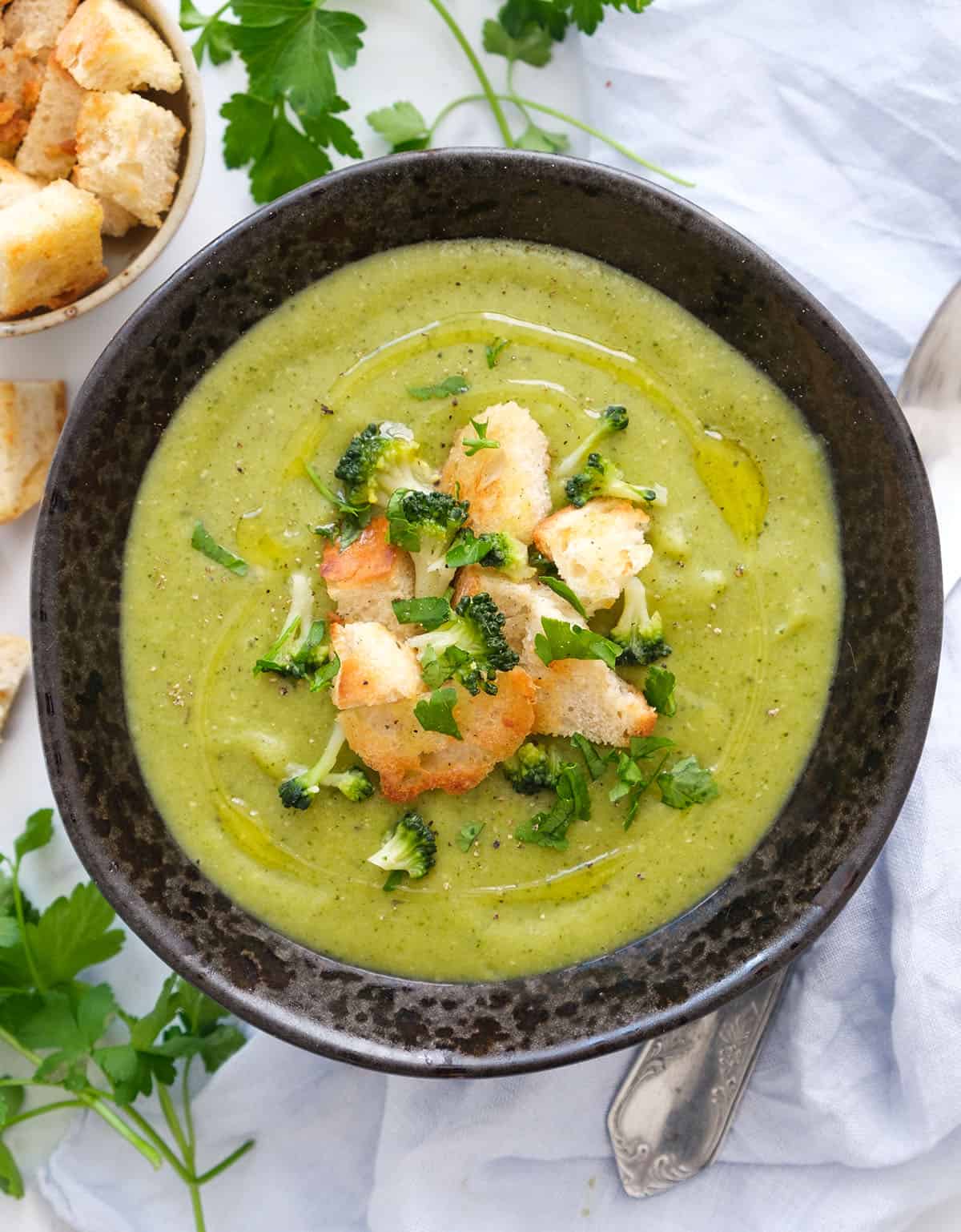 Top view of a dark bowl full of vegan broccoli soup garnished with golden croutons.