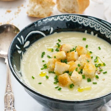 A dark bowl full of creamy vegan celeriac soup served with croutons and chopped chives.