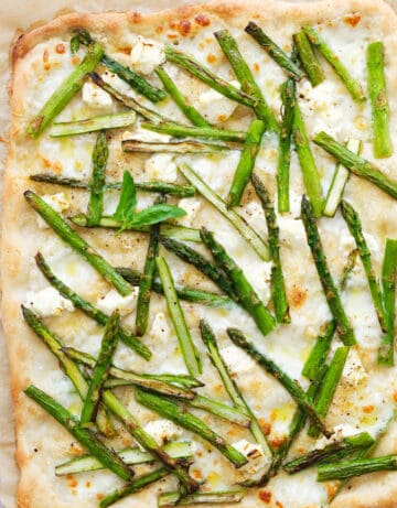 Top view of a large asparagus pizza with creamy mozzarella, cream cheese and fresh basil.