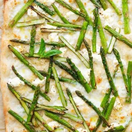 Top view of a large asparagus pizza with creamy mozzarella, cream cheese and fresh basil.
