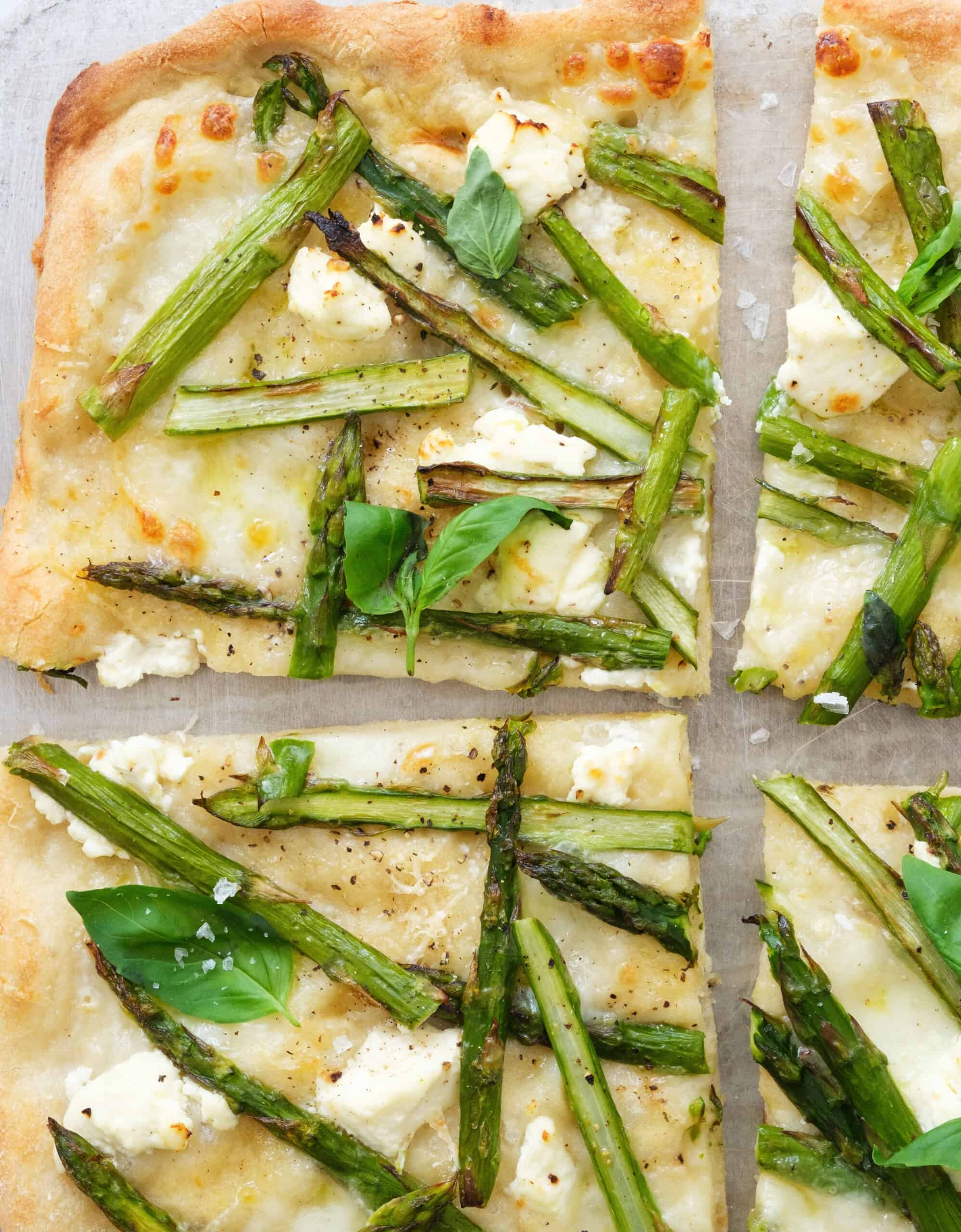 Close-up of few slices of asparagus pizza showing creamy cheese and crispy crust.