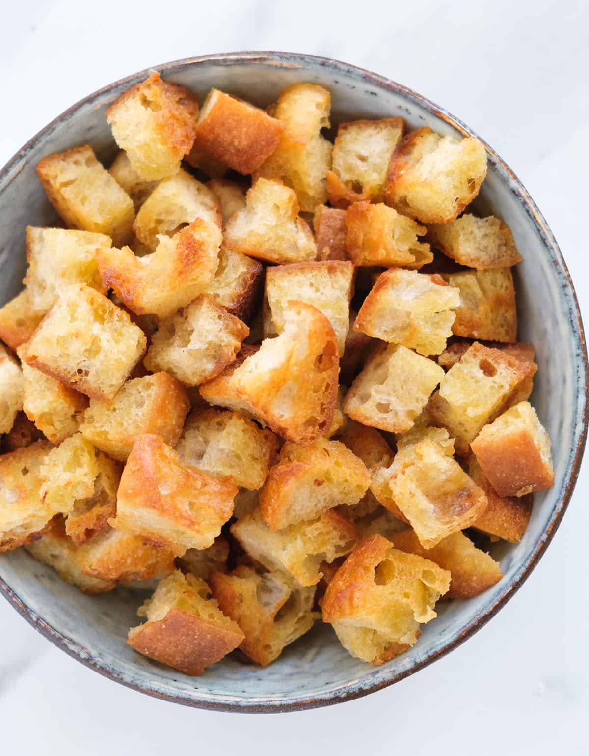 Top view of a bowl full of crispy croutons made in a pan over a white background.