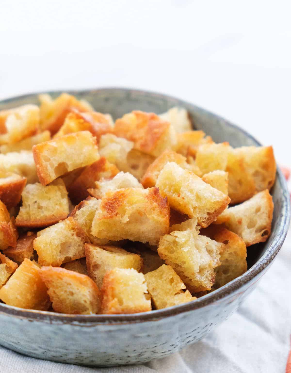 Close-up of a grey bowl full of golden croutons made on the stove over a white background.