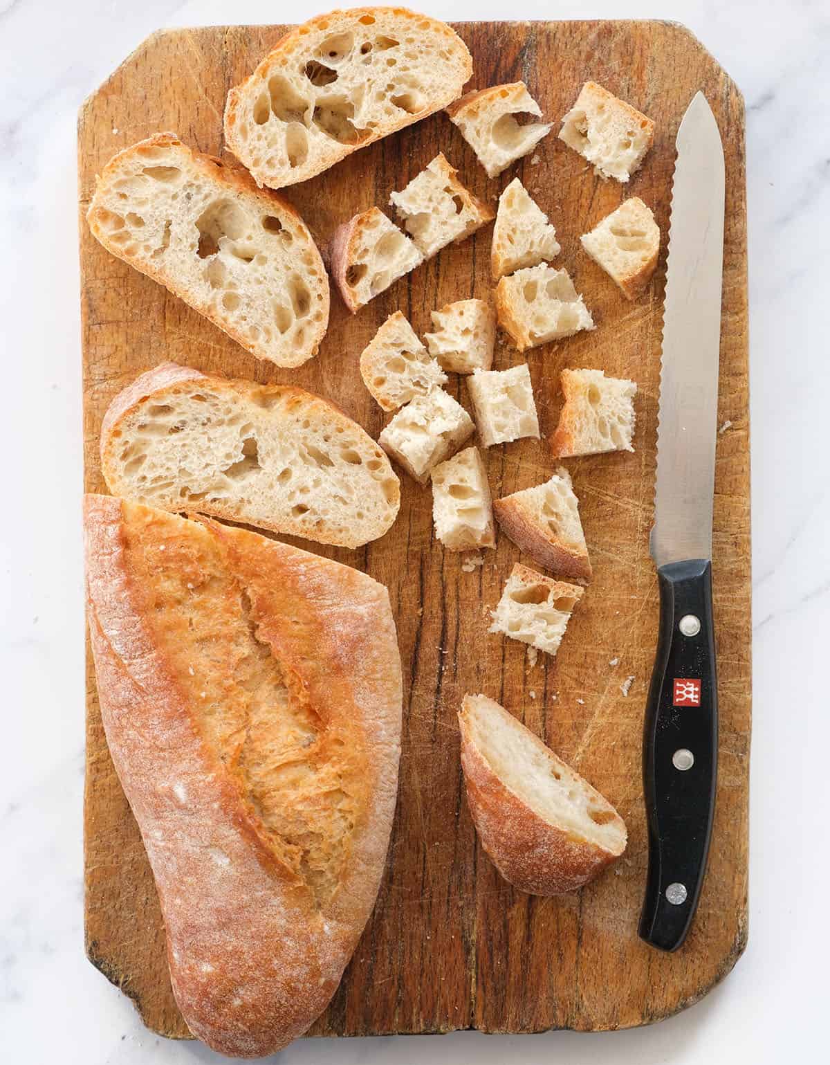 Top view of a wooden chopping board with rustic ciabatta bread cut into cubes.
