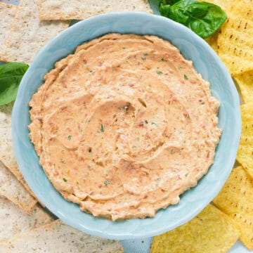 Top view of a turquoise bowl full of sun dried tomato cream cheese served with tortilla chips.