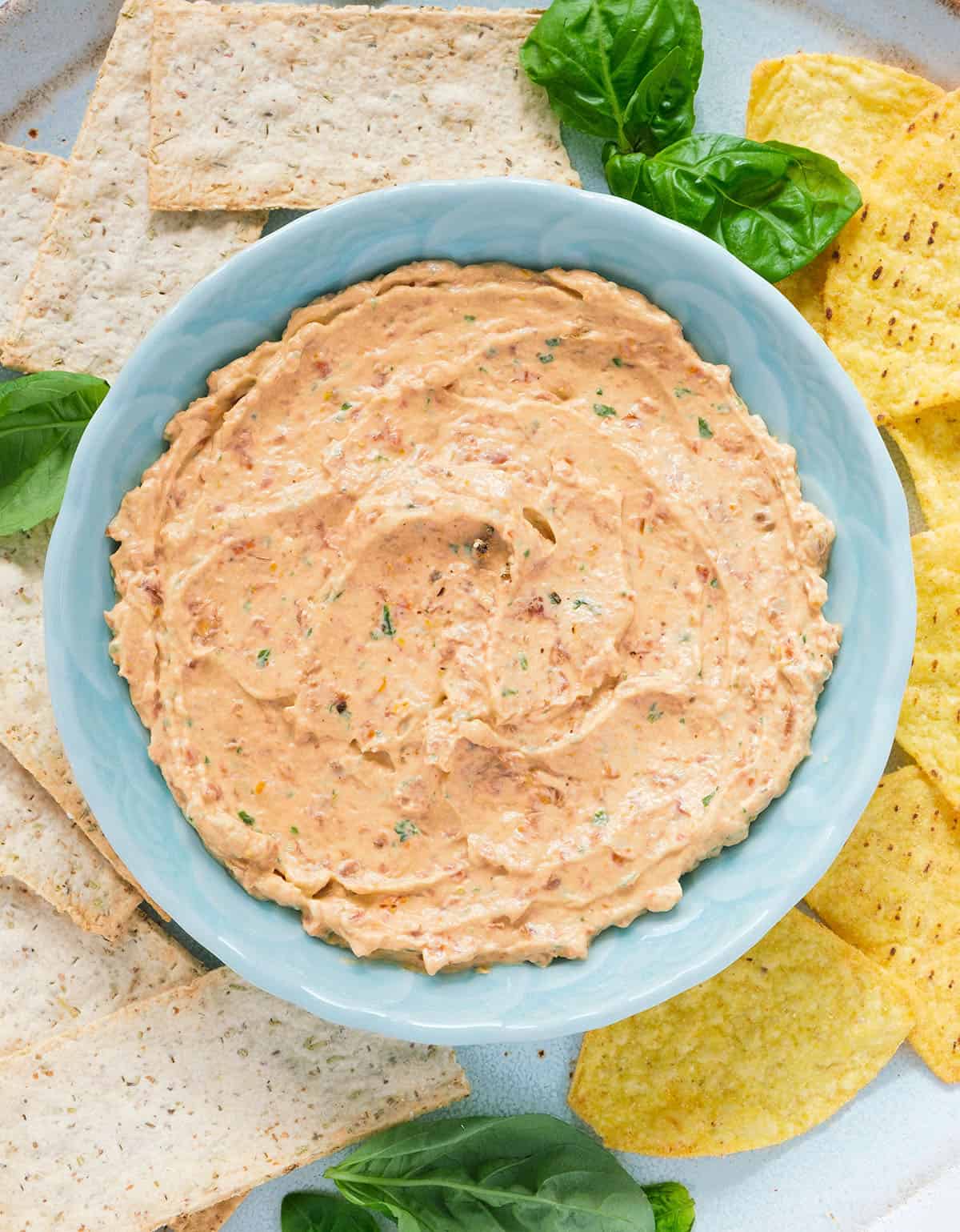 Top view of a turquoise bowl full of sun dried tomato cream cheese served with tortilla chips.