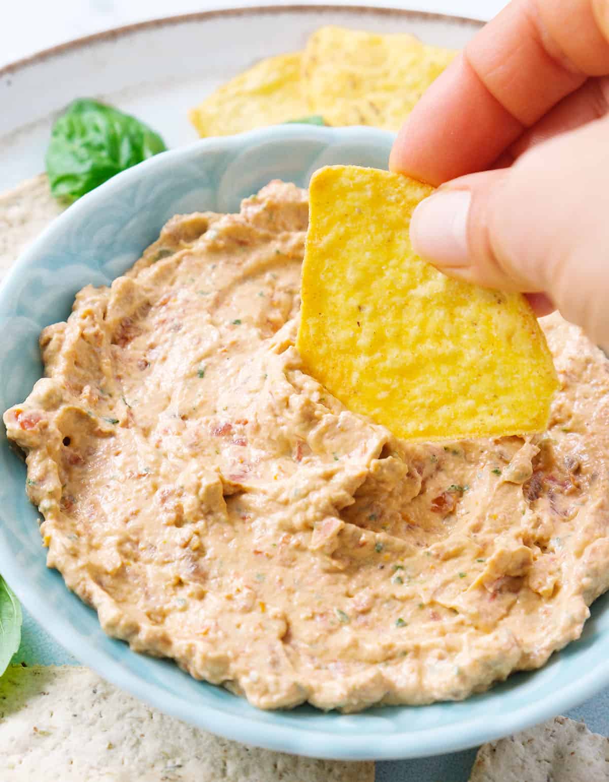 Close-up of a turquoise bowl full of sun dried tomato cream cheese served with tortilla chips.