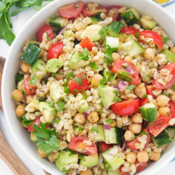 Top view of a white bowl full of vegan barley salad with tomatoes and avocado.