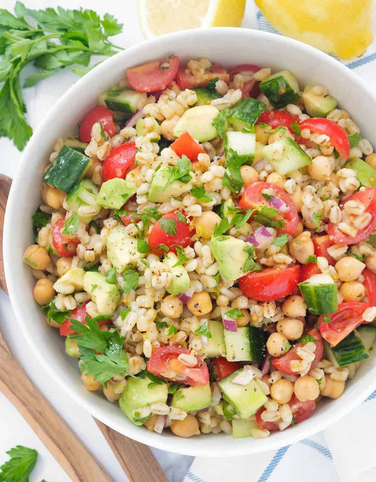 Top view of a vegan salad recipe made with barley, cherry tomatoes, cubed avocado and served in a white bowl.