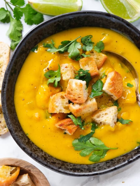 Top view of a black bowl full of creamy vegan sweet potato soup served with croutons and cilantro.